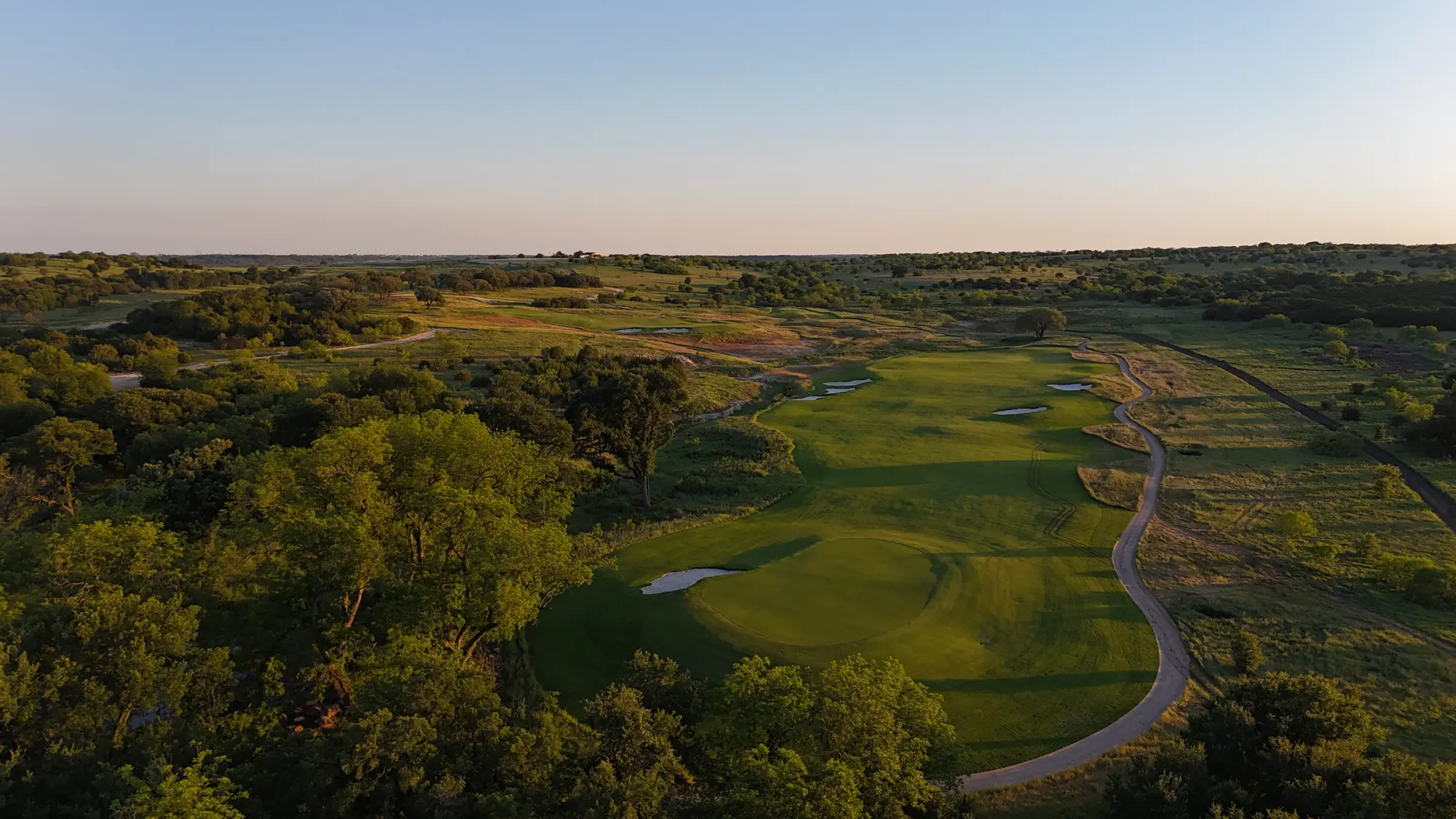 Aerial view at sunset of a green on the championship course, surrounded by trees