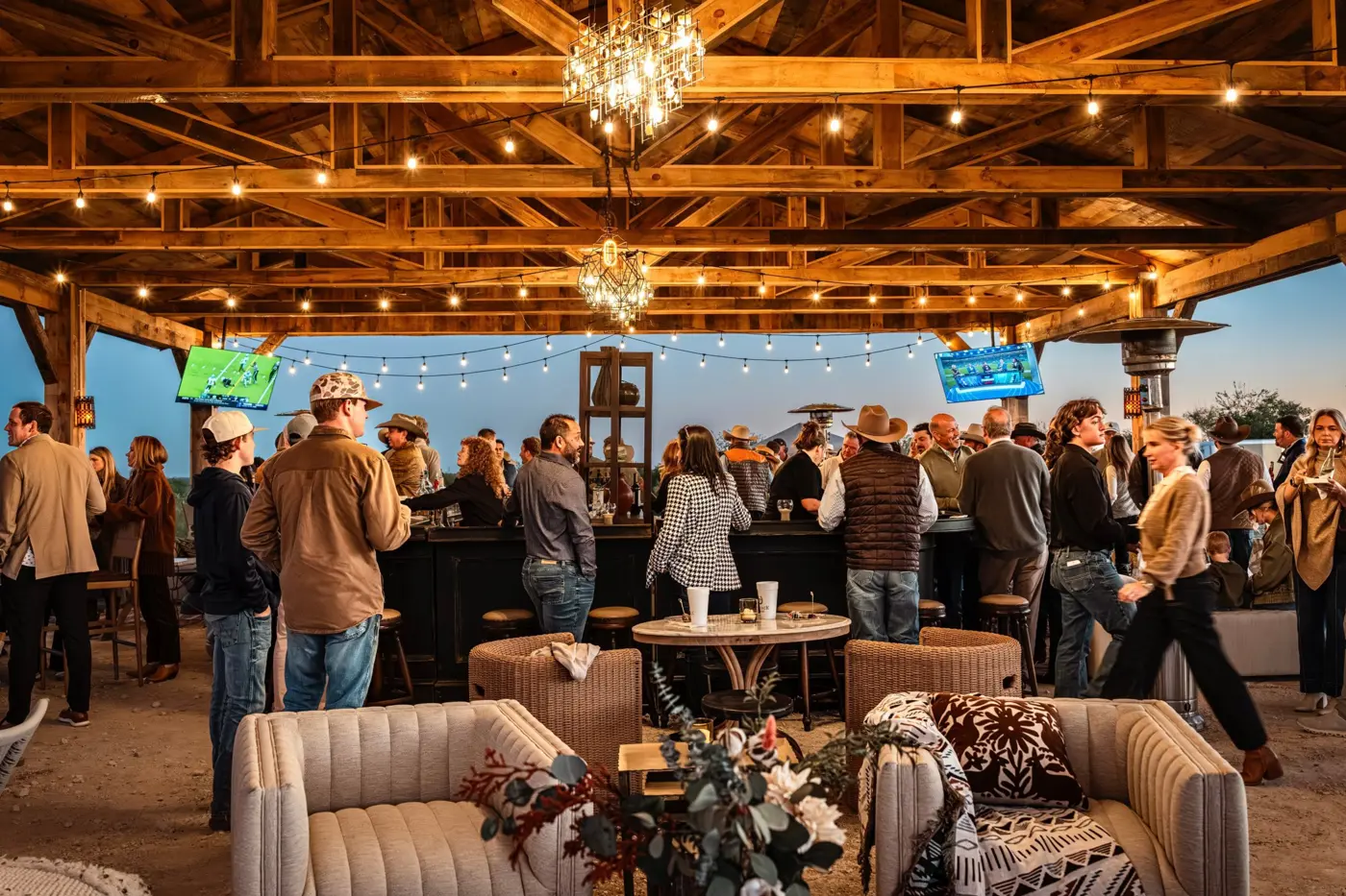Guests gathered at the bar under a timber pavilion with string lights at dusk